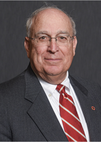 old man in a suit and red tie with glasses smiling